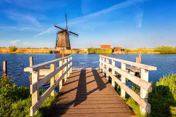 Famous Kinderdijk village of mills, popular tourist attraction in Netherlands (Holland), outdoor travel background. Scenic landscape with windmill, bridge, water, green grass and blue sky with clouds