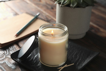 Burning candle in glass jar, succulent and notebook on wooden background, close up - obrazy, fototapety, plakaty