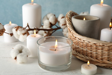 Burning candles, basket and cotton on white wooden table, close up