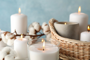 Burning candles, basket and cotton against blue background, close up