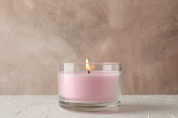Pink candle in glass jar on white table against brown, copy space