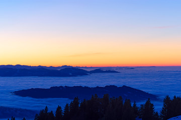 Colorful sky at sunset. Hills and forest sticking out of fog. Austria, Switzerland. Copy space