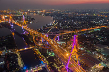 Evening bridge with lights on the bridge over the Chao Phraya River. Aerial view of the Bhumibol Adulyadej Suspension Bridge over the Chao Phraya River in Bangkok with cars on the bridge at the sunset