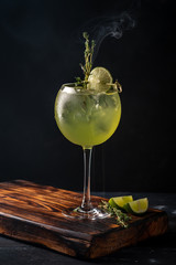 Refreshing Cocktail with Basil Leaf, Lime and ice in a wine glass on a dark background. drink gin...