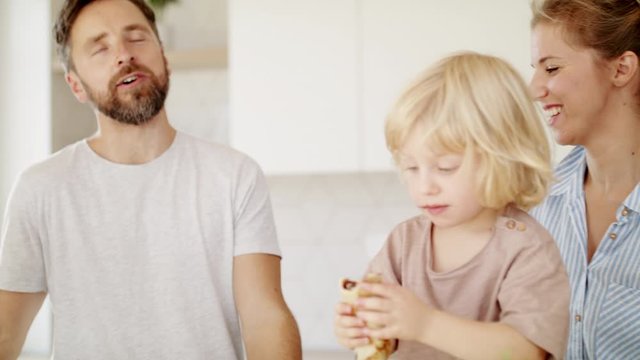 Young family with two small children indoors in kitchen, eating pancakes.