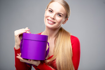 Young blonde woman with beautiful healthy long hair and natural make up holds a gift box. Fashion beauty portrait