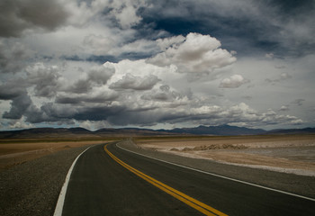Pov. Empty asphalt highway in the desert under a dramatic cloudy sky in the Andes mountain range