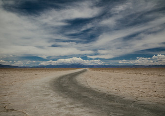 Fototapeta na wymiar Dirt Road in the desolated salt flat desert, Salinas Grandes, Jujuy, Argentina, under a beautiful cloudy sky
