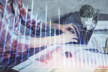 Double exposure of stock graph with businessman typing on computer in office on background. Concept of hard work.