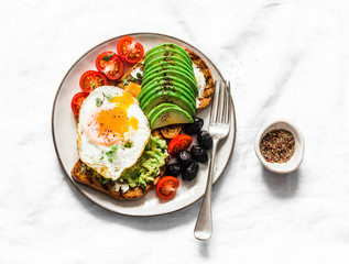 Delicious brunch - fried egg, avocado, grilled bread, dried olives, cherry tomatoes. Delicious healthy breakfast, snack on a light background, top view