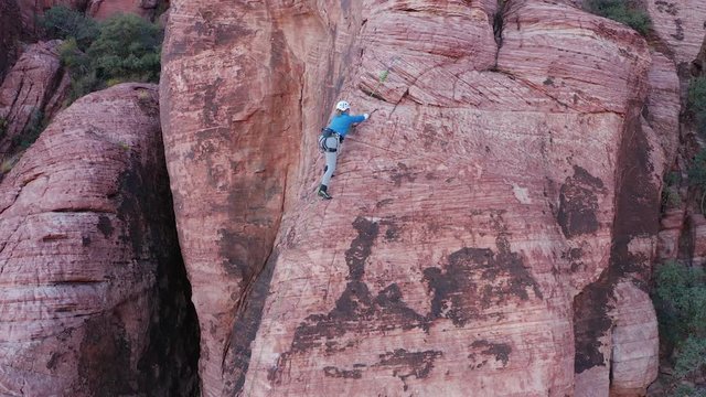 Aerial zoom in shot of female rock climber climbing and reaching the anchors 