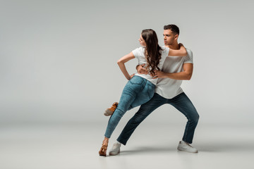 dancers in t-shirts and jeans dancing bachata on grey background