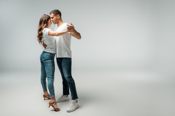 smiling dancers in t-shirts and jeans dancing bachata on grey background