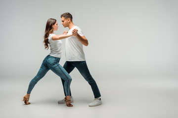 side view of dancers in t-shirts and jeans dancing bachata on grey background