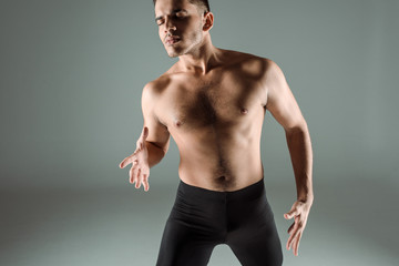 Fototapeta na wymiar handsome dancer with closed eyes in black leggings dancing contemporary on grey background