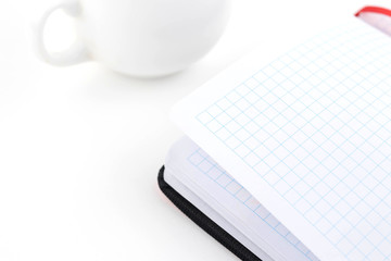 Open notebook and cup of coffee on a white background .on an office desk