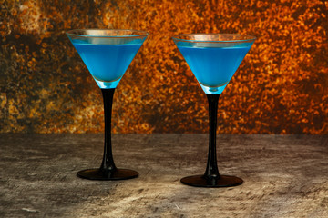 Blue cocktail in martini glasses with ice on a gray concrete background. Blue cocktail with martini on a gray stone background with lemon.