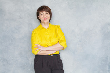 Happy mature business woman in yellow shirt smiling and standing with crossed arms