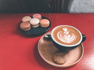 Latte art coffee in ceramic mug on wooden table.Warm drink eaten together with a slightly sweet Macaron.