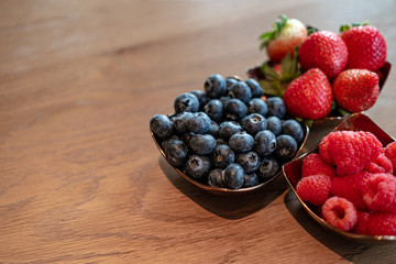 Fresh raspberries , blueberries, strawberry in the copper bowls on rustic natural wooden background
