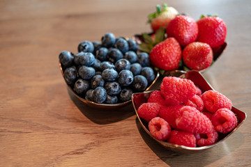 Fresh raspberries , blueberries, strawberry in the copper bowls on rustic natural wooden background
