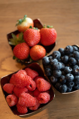 Fresh raspberries , blueberries, strawberry in the copper bowls on rustic natural wooden background