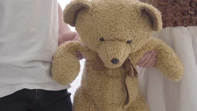 Close-up of little male and female Caucasian hands holding teddy bear together. Soft toy shared by two friends. Childhood, leisure, playfulness.