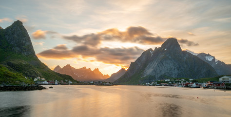 Fototapeta na wymiar Panorama shot of Reine in Lofoten Islands in Norway during sunset. Warm tones and colors fills the cloudy sky during summertime. Travelocity and traveling concept.