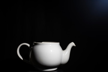 Photo of a white ceramic kettle with shadows from light and a black background.