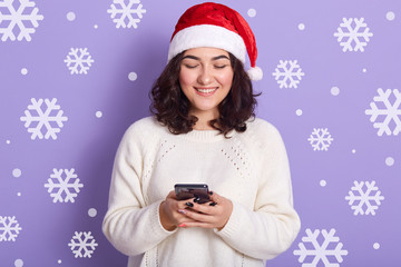 Horizontal studio picture of cheerful beautiful black haired woman chatting over phone, holding...