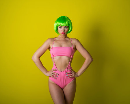 Beautiful woman in a green short wig and pink bikini posing on a yellow background. Portrait of a girl with sensual red lips.