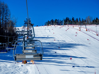 Ski lifts (chairlift and ski tow), and ski slope with slalom gates for skiers and snowboarders in...