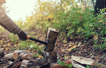 Man cuts a log with an industrial ax. Parts of the tree fly apart. A strong man holds an ax in his hands on a background of forest, firewood. A man lumberjack with an ax in his hand