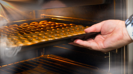 Female hand putting baking tray with vanilla rolls to open hot steaming oven. Stacked crescent...