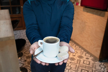 manos de hombre sosteniendo taza de cafe americano en una cafeteria