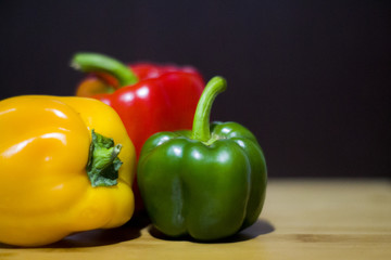 tres pimentones de diferentes colores en tabla de madera con fondo negro