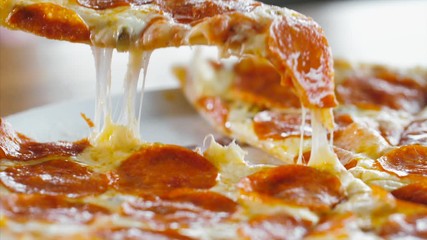 Hand taking salami pizza slice via spatula. Hot melted cheese is stretching, close-up. Fast-food concept.