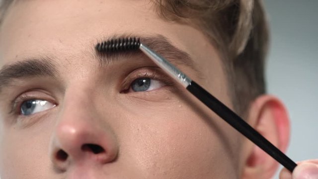 Macro of young attractive man upper face and eyebrow brush brushing his eyebrow