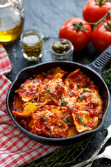 Ravioli with tomato sauce sprinkled with Parmesan cheese and herbs in a cast iron skillet on a black background close up