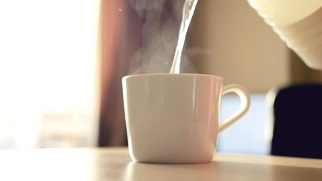 Pour boiling water from a teapot into a white cup early in the morning. Spray is flying in all directions. HD, 1920x1080, slow motion
