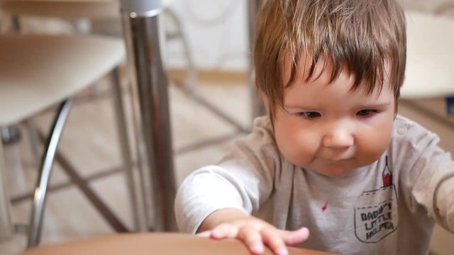 The child learns to walk on the wall. A small child learning to walk, holding on to a wall in a room. The kid is laughing with new baby teeth. The first steps. The joy of the child from the first step
