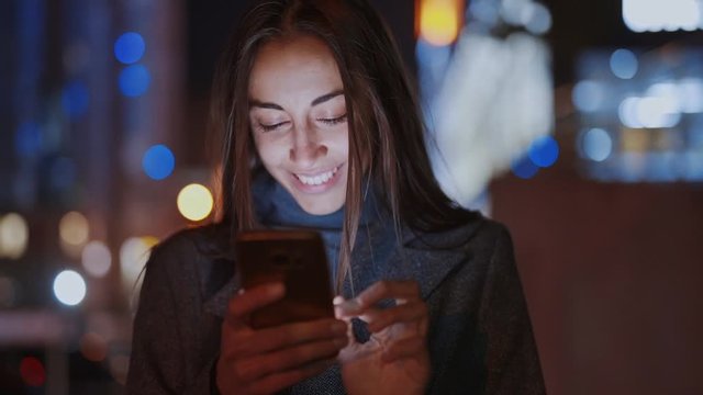 Closeup of prety smiling woman using smartphone walking at night city, slowmotion fullHD stock footage, handheld camera shot