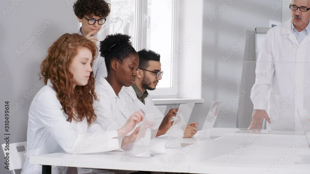 Poster medium shot of diverse young students in lab coats working on futuristic interactive touchscreen com