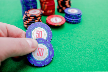 Hand holding two chips for betting on poker next to a stack of different value chips on a green game table
