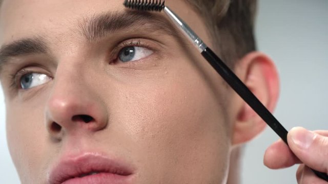 Macro of young attractive man face and eyebrow brush shaping his eyebrow