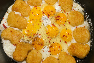 Fried eggs and nuggets in a pan. Breakfast of omelet with chicken.