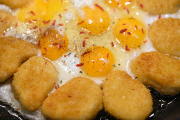 Fried eggs and nuggets in a pan. Breakfast of omelet with chicken.