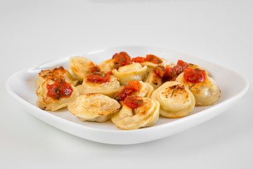 Russian food pelmeni, fried meat dumplings on white plate, with tomato sauce, isolated