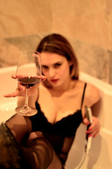 Beautiful girl in black bodysuit lies in the bath with a glass in her hands