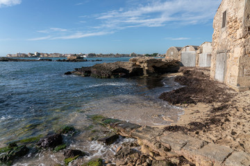 Old fishermen's stone traditional huts in the Majorcan cove of Can Curt, with sand and rocks, in the background Colonia de Sant Jordi village.